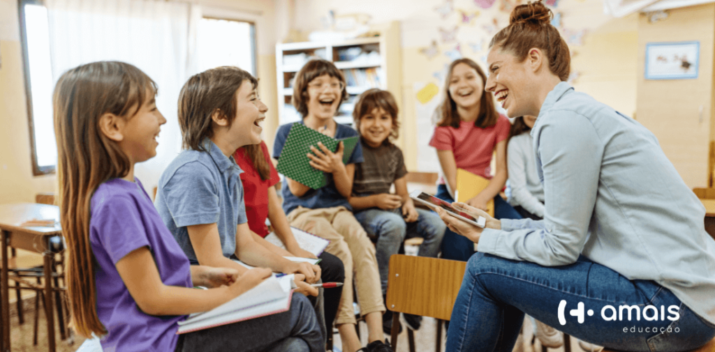 Professora e crianças em sala de aula sentadas em cima das mesas em forma de roda se divertindo ao aprender bilinguismo e desenvolvimento socioemocional