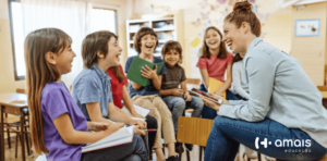 Professora e crianças em sala de aula sentadas em cima das mesas em forma de roda se divertindo ao aprender bilinguismo e desenvolvimento socioemocional